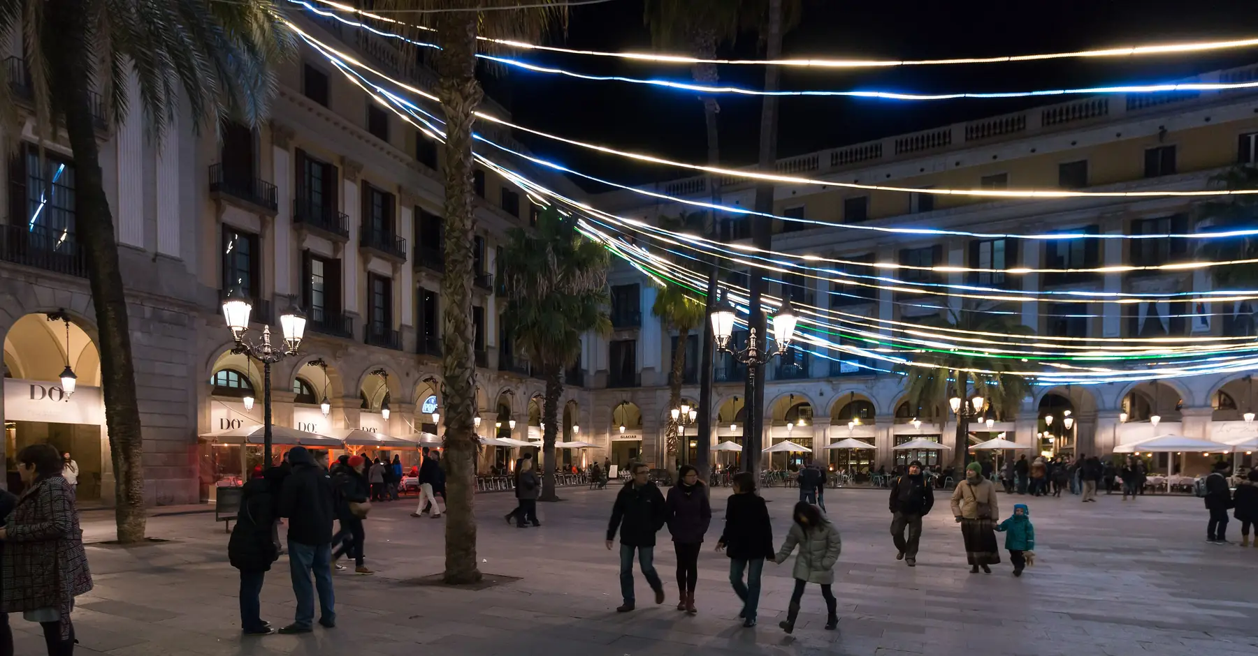 Plaça Reial at night, with strings of lights stretched between palm trees over a square of street lamps and arcaded buildings